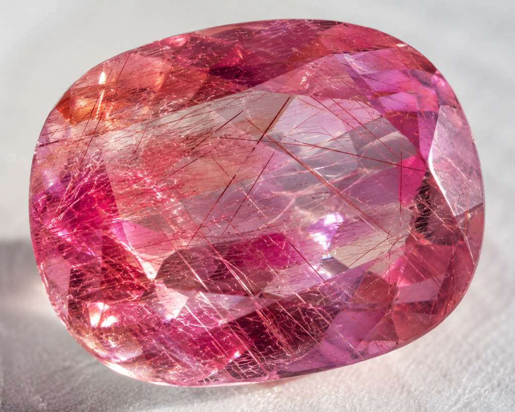 Close-up macro shot of a faceted pink gem with natural color zoning and visible rutile needle inclusions, showcasing the unique internal structure of a rare pink gem under daylight.pink gems